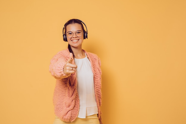 A morena alegre nos vidros e nos fones de ouvido vestiu-se na blusa branca da camiseta cor-de-rosa e no sorriso largo das calças amarelas, apontando a câmera sobre o fundo amarelo com espaço da cópia. Positivo e jovem.