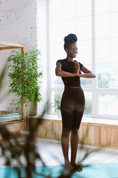 A mulher afro-americana calma e meditativa vertical faz ioga mantém as mãos em namaste asana Estilo de vida ativo e saudável