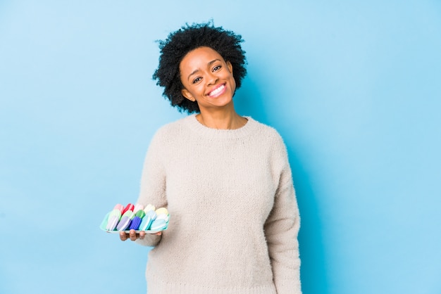 A mulher afro-americano da Idade Média que come os bolinhos de amêndoa isolou feliz, sorridente e alegre.