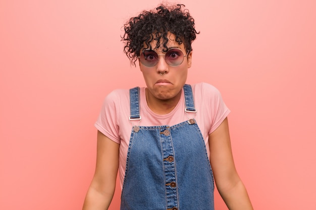 Foto a mulher afro-americano misturada nova do adolescente encolhe os ombros e abre os olhos confusos.