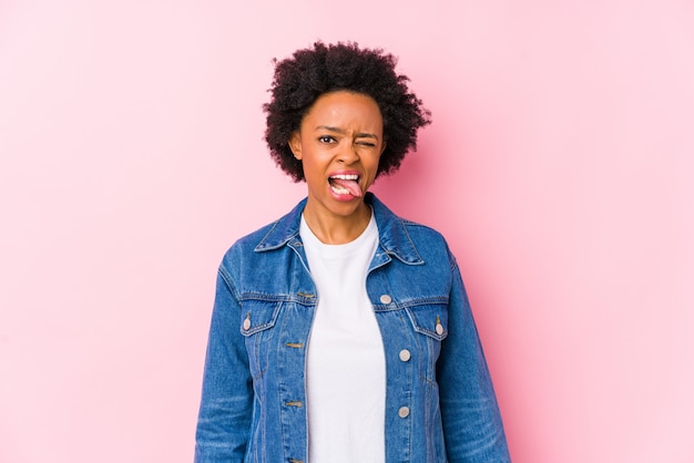 A mulher afro-americano nova contra um backgroound cor-de-rosa isolou engraçado e amigável saindo da língua.