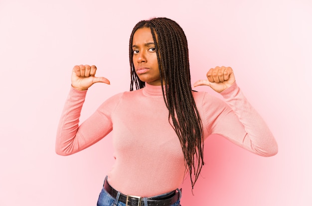 A mulher afro-americano nova isolada em uma parede cor-de-rosa sente orgulhosa e auto-confiante, exemplo a seguir.