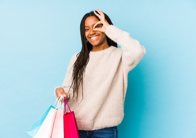 A mulher afro-americano nova que guarda um saco de compras excitou mantendo o gesto aprovado no olho.