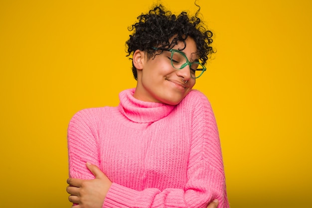 A mulher afro-americano nova que veste uma camisola cor-de-rosa abraça, sorrindo despreocupado e feliz.