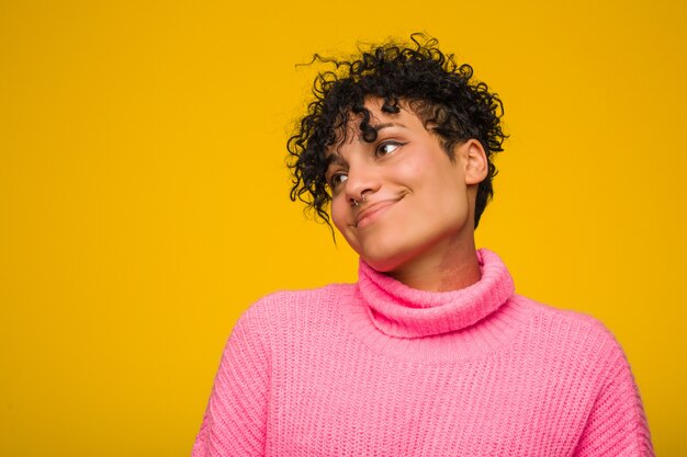 A mulher afro-americano nova que veste uma camisola cor-de-rosa toca na barriga, sorri delicadamente, comendo e conceito da satisfação.