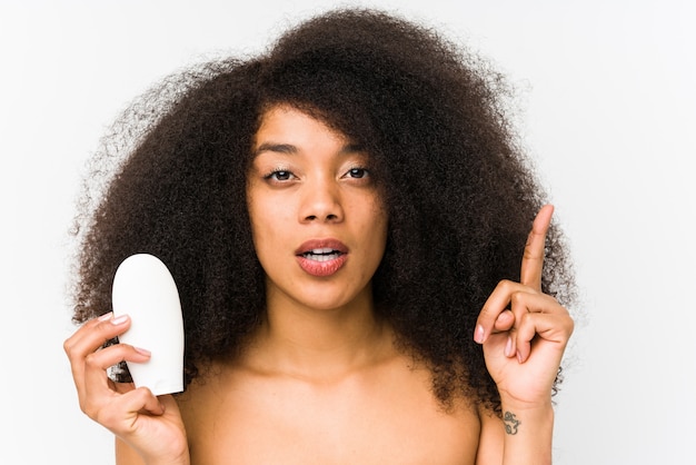 A mulher afro nova que mantem um creme hidratante isolado tendo alguma grande ideia, conceito da faculdade criadora.