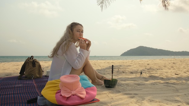 A mulher alegre em segurar e comer fatias de melancia no mar de praia de areia tropical. garota atraente de retrato passa o fim de semana de verão.