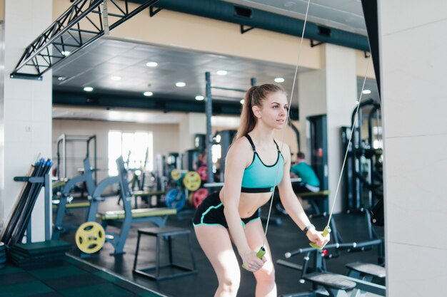 A mulher alegre no sportswear se exercita na máquina de simulação do esquiador no ginásio.