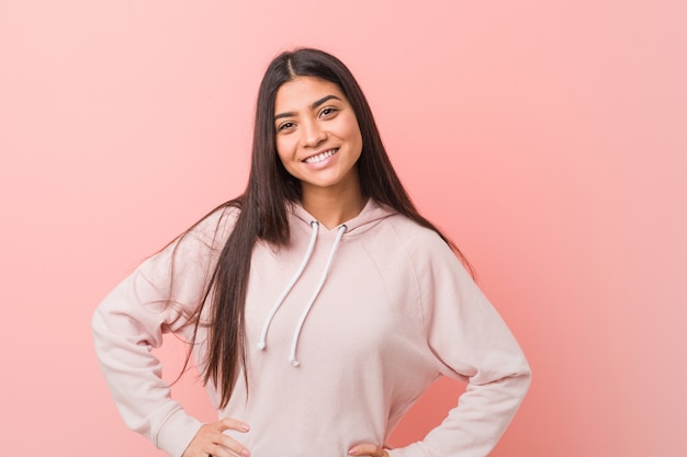 A mulher árabe bonita nova que veste um esporte ocasional olha segura mantendo os quadris das mãos.