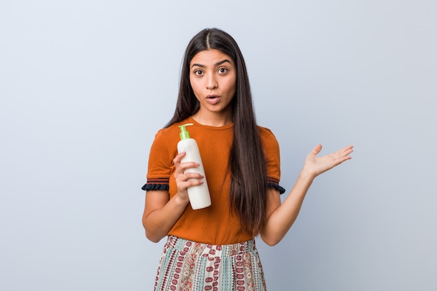 A mulher árabe nova que guarda uma garrafa de creme imprimiu guardar o espaço da cópia na palma.