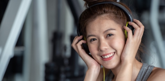 Foto a mulher asiática do esporte com fones de ouvido que escuta a música relaxa após o exercício duro do exercício no gym do esporte.