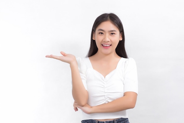 A mulher asiática do retrato está sorrindo e mostra as mãos para apresentar algo no fundo branco