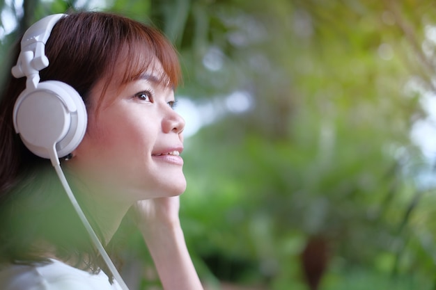 A mulher asiática escuta música com auscultadores em casa. Face lateral que olha com espaço da cópia.