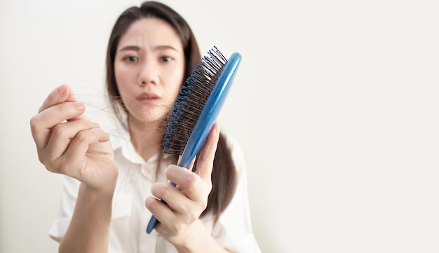 A mulher asiática está procurando perda de cabelo e usa a mão para remover o cabelo do pente com um preocupado e infeliz