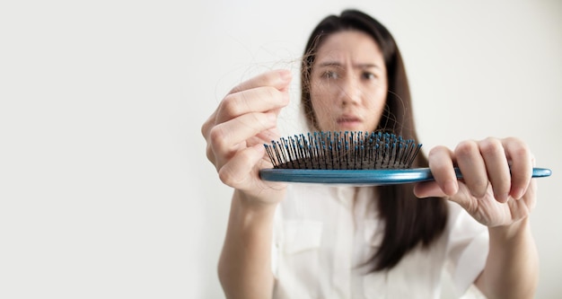 Foto a mulher asiática está procurando perda de cabelo e usa a mão para remover o cabelo do pente com um preocupado e infeliz