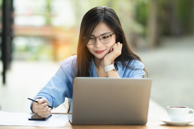 A mulher asiática está trabalhando no computador pessoal e no smartphone na internet trabalhando em casa