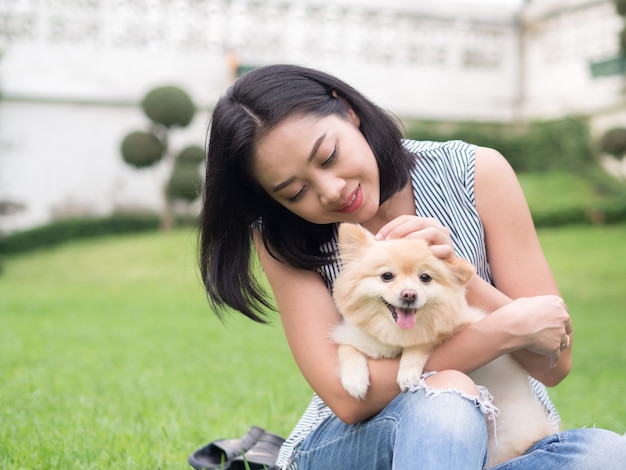 A mulher asiática joga com seu cachorrinho pomeranian no jardim.