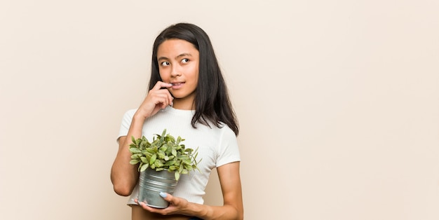 A mulher asiática nova que guarda uma planta relaxou o pensamento sobre algo que olha um espaço da cópia.