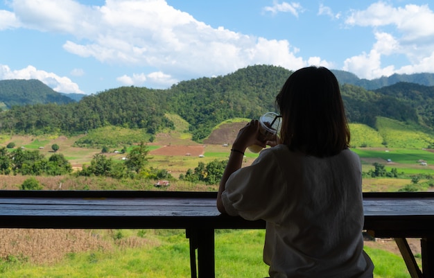 A mulher asiática senta e bebe o café.