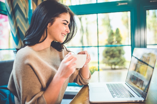 A mulher atraente com um laptop toma um café no café