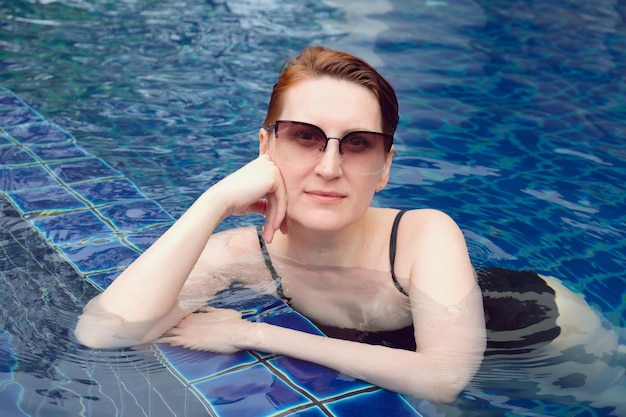 A mulher bonita com cabelo vermelho curto está relaxando na piscina