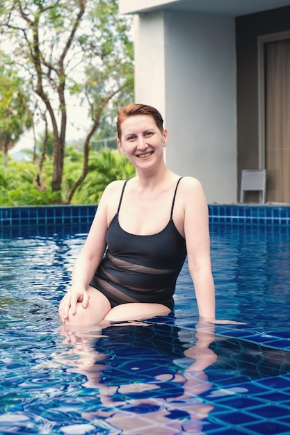 A mulher bonita com cabelo vermelho curto está relaxando na piscina