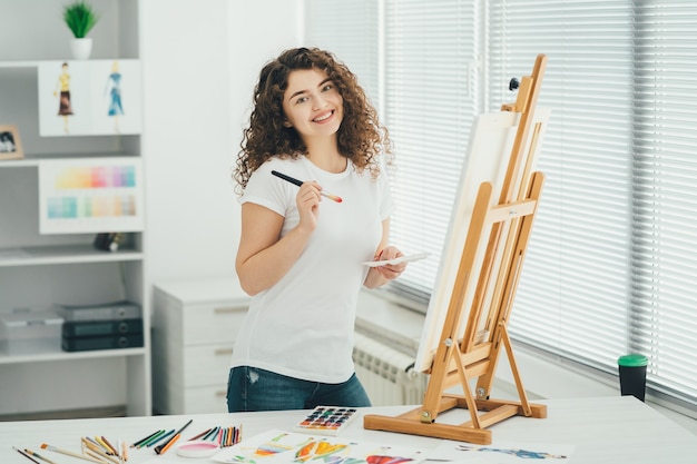 A mulher bonita com um pincel de arte pintando um quadro no cavalete