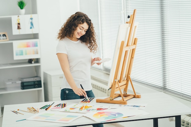 A mulher bonita com um pincel de arte pintando um quadro no cavalete