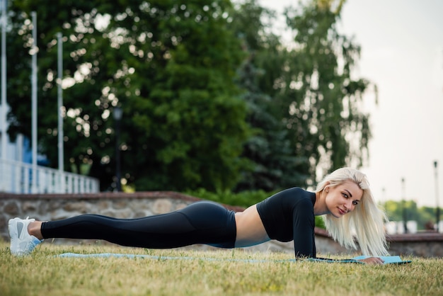 A mulher bonita da aptidão em um esporte veste fazer o exercício da prancha ao ar livre. estilo de vida saudável do esporte