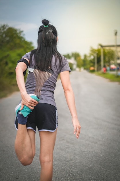 A mulher bonita de Ásia em mercadorias do esporte aquece-se antes de correr na estrada.