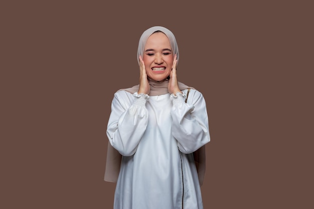 A mulher bonita no hijab fechou os olhos enquanto segurava as bochechas isoladas no fundo liso
