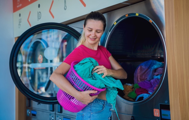 A mulher bonita nova lava e seca a roupa na lavanderia