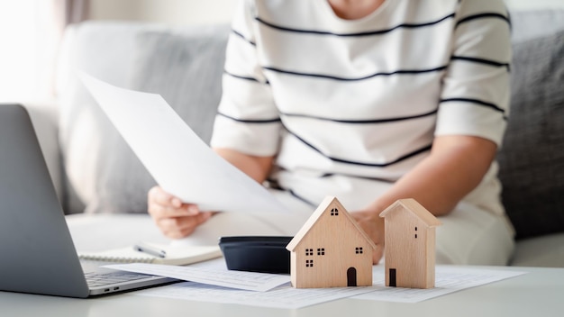 A mulher calcula a hipoteca do empréstimo à habitação para resumir os pagamentos de despesas com o modelo de casa de madeira pequena