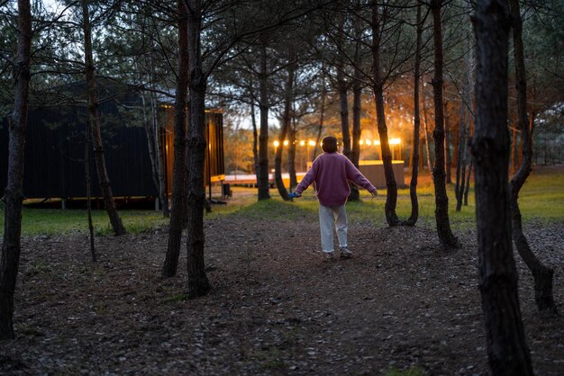 A mulher caminha na floresta de pinheiros perto da cabana de madeira ao entardecer