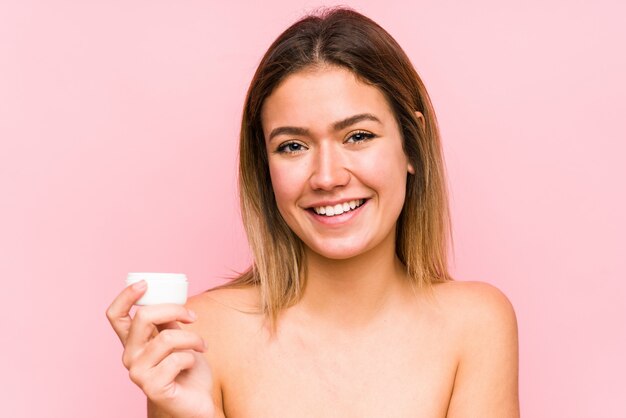 A mulher caucasiano nova que guarda um creme hidratante isolou feliz, sorrindo e alegre.