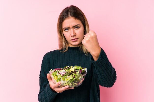 A mulher caucasiano nova que guarda uma salada isolou mostrar com expressão facial agressiva.