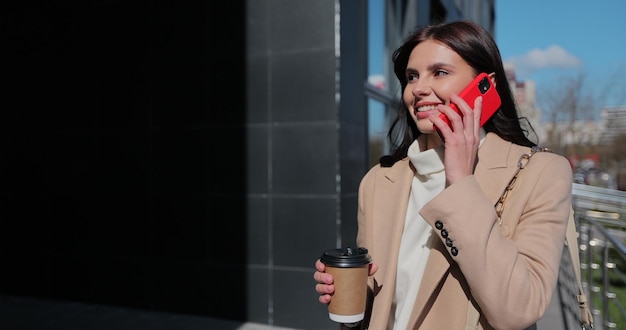A mulher chega perto do prédio de escritórios e fala ao telefone A jovem faz uma pausa enquanto trabalha com café na rua