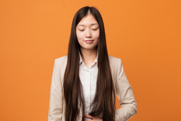 A mulher chinesa do negócio novo toca na barriga, sorri delicadamente, comendo e conceito da satisfação.