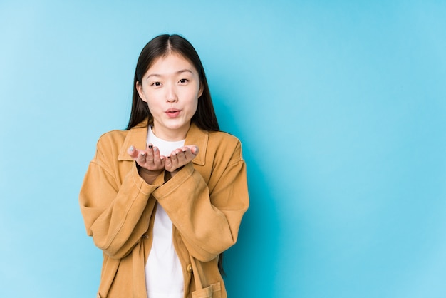 A mulher chinesa nova que levanta em uma parede azul isolou os bordos de dobramento e guardar as palmas para enviar o beijo do ar.