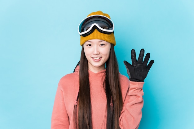 A mulher chinesa nova que veste o esqui veste o número mostrando alegre de sorriso cinco com dedos.