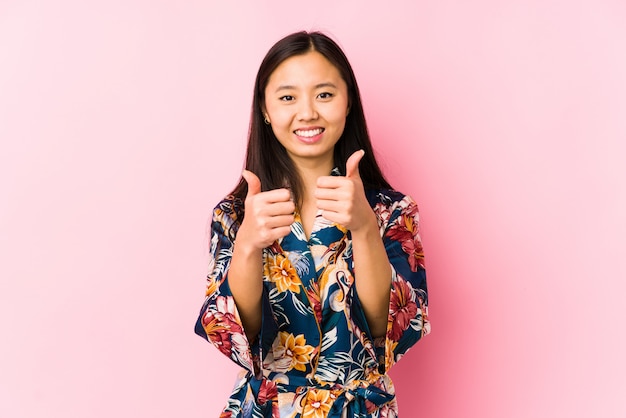 A mulher chinesa nova que veste um pijama do quimono isolado com polegares levanta, elogios sobre algo, apoia e respeita o conceito.