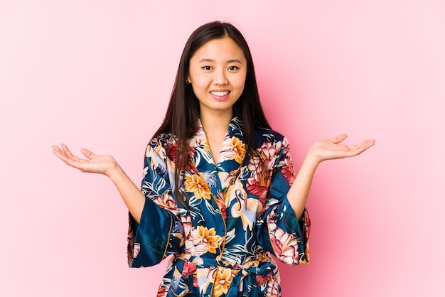 A mulher chinesa nova que veste um pijama do quimono isolado faz a escala com braços, sente-se feliz e confiante.