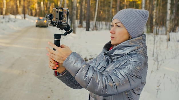 A mulher cinegrafista profissional segurando smartphone no dispositivo de estabilização de gimbal de 3 eixos no inverno equipamento profissional ajuda a fazer vídeo de alta qualidade no telefone operador de cinegrafista em câmera lenta