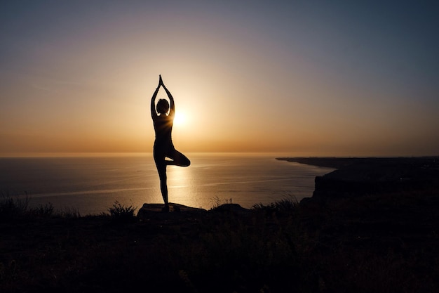 A mulher com postura de ioga na montanha ao pôr do sol.