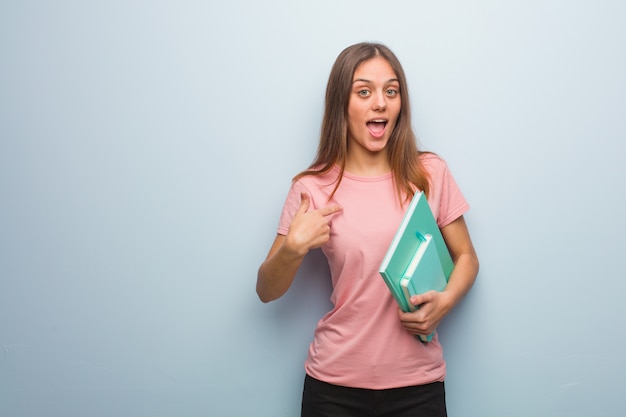 A mulher consideravelmente caucasiano dos jovens surpreendida, sente bem sucedida e próspera. Ela está segurando livros.