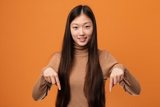 A mulher consideravelmente chinesa nova aponta para baixo com dedos, sentimento positivo.