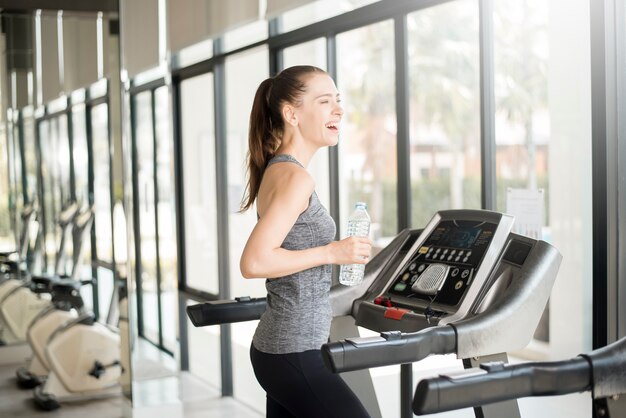 A mulher consideravelmente nova do esporte está bebendo a água na escada rolante na ginástica, estilo de vida saudável