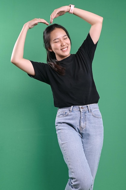 A mulher coreana sente-se feliz e romântica fazendo gestos em forma de coração contra um fundo verde