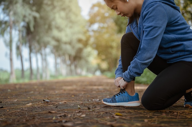 A mulher correndo amarrando cadarços de tênis antes de correr pela rua no parque natural