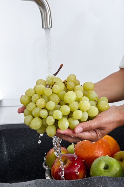 A mulher cozinheira lava um cacho de uvas na água que escorre de uma torneira.